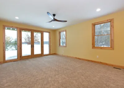 Empty room with carpet flooring, pale yellow walls, a ceiling fan, and sliding glass doors looking out to a snowy landscape.