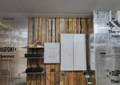 An unfinished utility room with exposed wall studs, an array of electrical wires, and installed electrical panels.