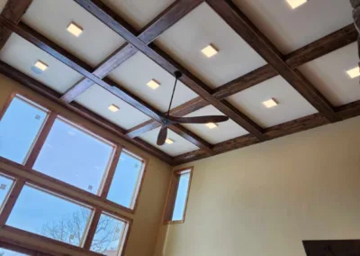 Vaulted ceiling with exposed wooden beams and recessed lighting in a room with large windows.