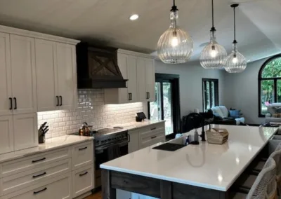 Modern kitchen interior with white cabinetry, a central island, pendant lights, and hardwood flooring.