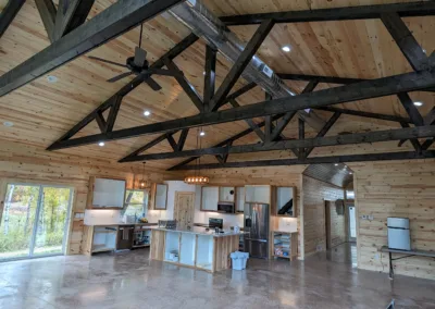 Spacious wooden interior of a house under construction with exposed beam ceiling and kitchen fixtures being installed.