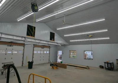 Industrial-style interior of a spacious workshop with fluorescent lighting, scattered tools, and a garage door.