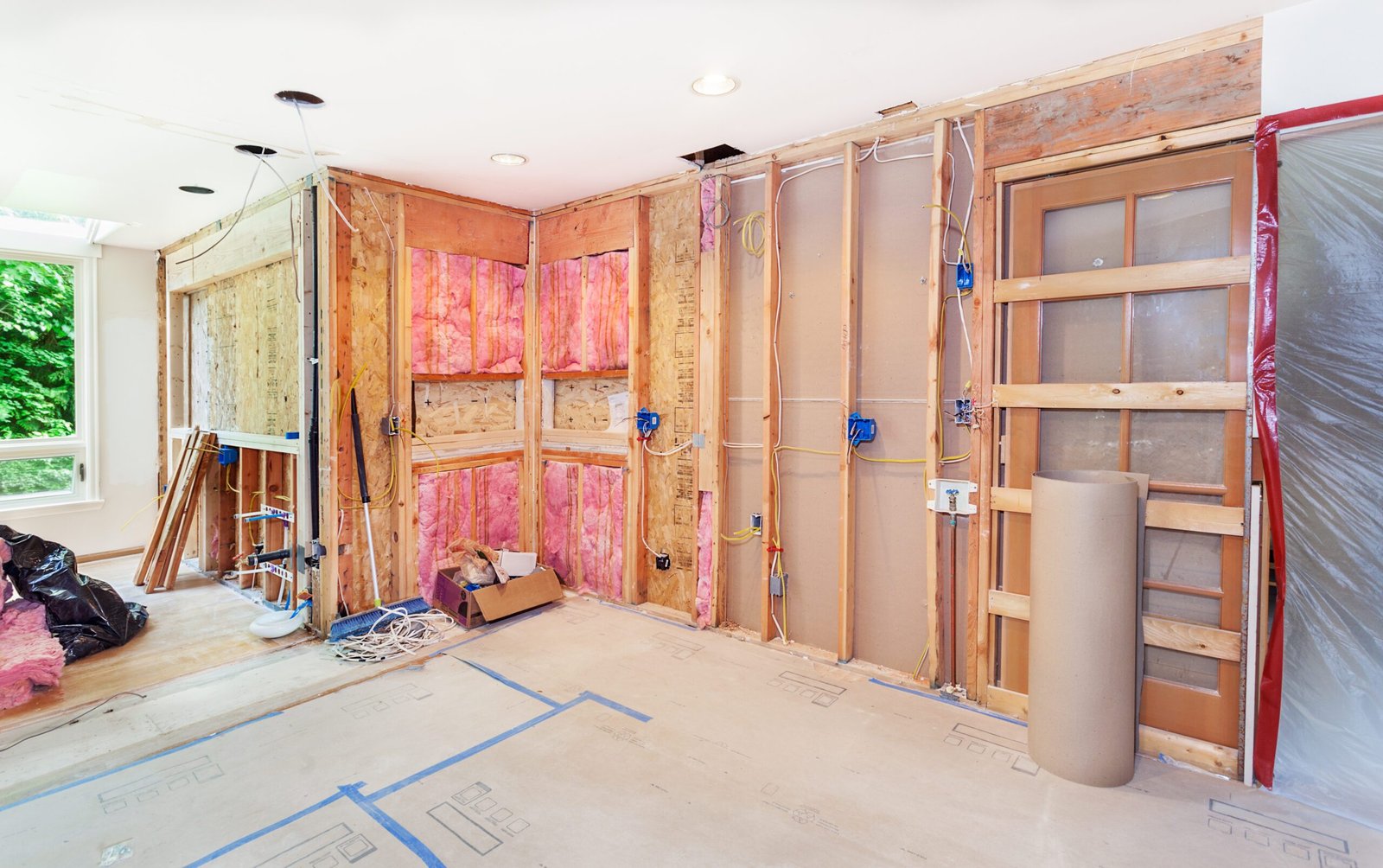 Interior of a house under renovation showing exposed insulation, wooden studs, and construction materials.