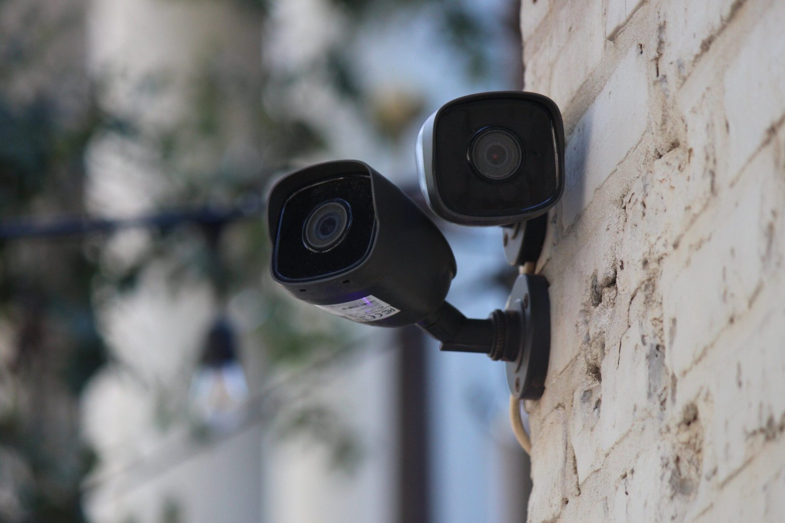 Two black security cameras mounted on a weathered beige wall, focusing in different directions.