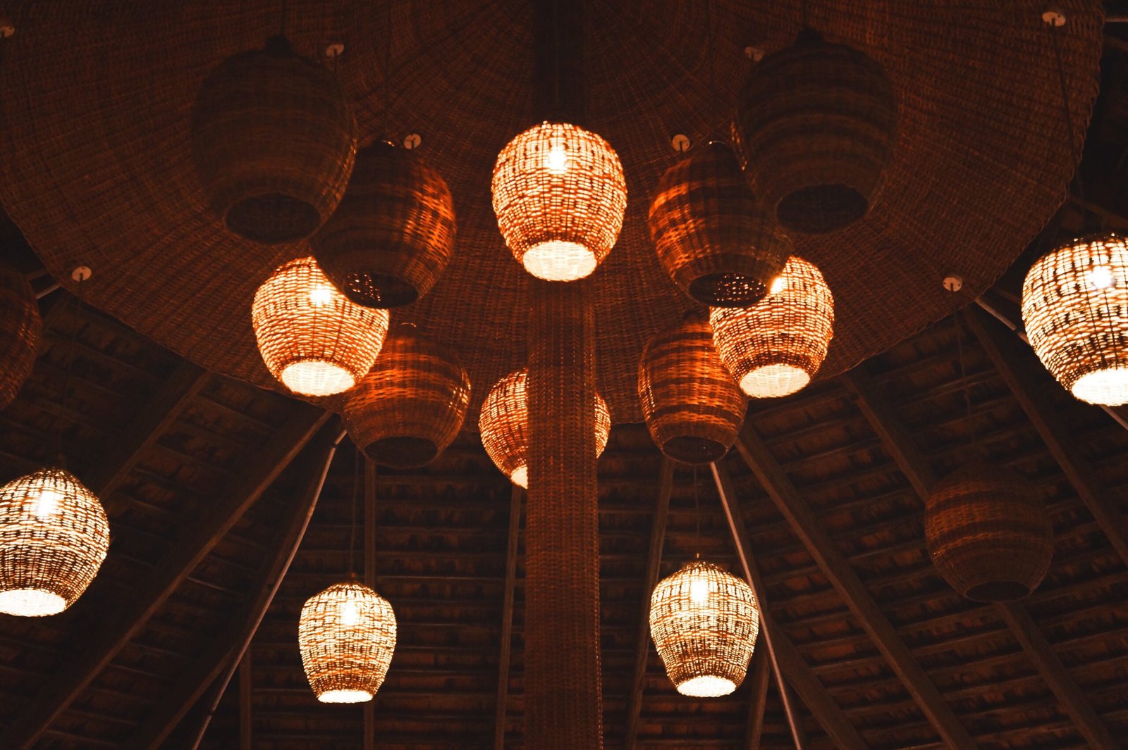 Warmly lit woven rattan pendant lights hanging from a wooden ceiling in a symmetrical arrangement.