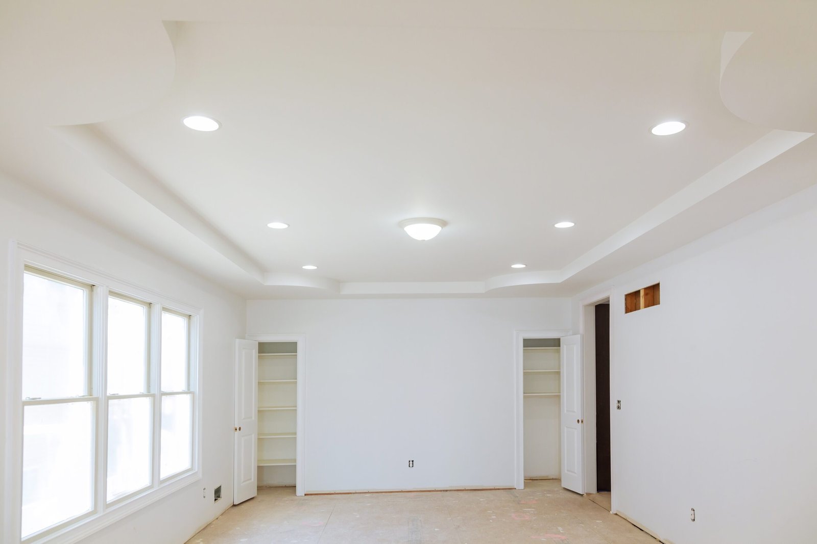 Bright, empty room with recessed lighting, built-in shelves, and large window, with hardwood floors and a white interior.