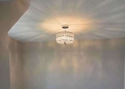 A ceiling light fixture with a patterned shade casts decorative shadows and light on a textured white ceiling and plain walls.
