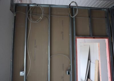 Metal wall studs with electrical wiring and outlet boxes installed; unfinished drywall leaning against the wall on the right side.