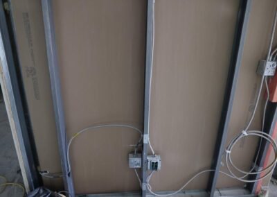 Exposed electrical wiring and metal studs on a wall under construction, with electrical boxes and conduit visible.